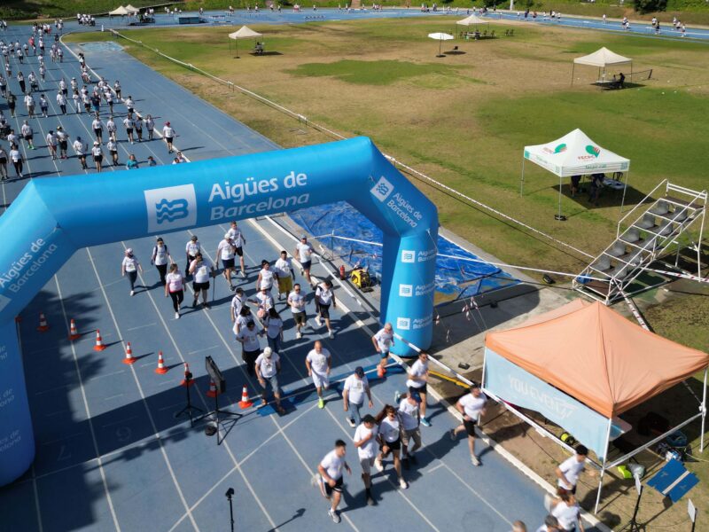 Fotografía panorámica de la carrera de las capacidades en Barcelona. Aparece n los participantes corriendo y atravesando el arco de meta hinchable de la pista de atletismo.